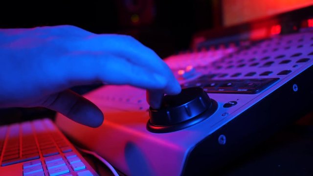 Sound engineer rotates the scroll wheel on mixing console in a professional recording studio. Musician working on new song. Slow motion. 4k. Neon light.
