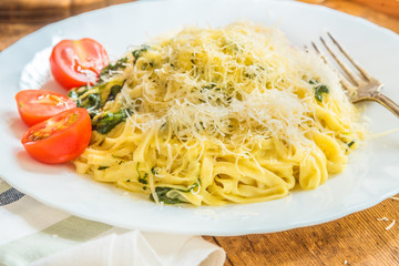 Delicious vegetarian pasta with spinach cream sauce on a white plate with cherry tomatoes