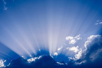 Fototapeta na wymiar Sunbeams rising from a large cloud in intense blue sky on a summer afternoon