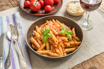 Pasta All'Arrabbiata, penne with tomato sauce, basil, parmesan cheese and red wine on a rustic wooden table with linen napkin