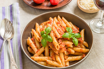 Pasta All'Arrabbiata, penne with tomato sauce and basil and parmesan cheese on a rustic wooden table with linen napkin