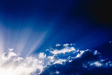 Sunbeams rising from a large cloud in intense blue sky on a summer afternoon