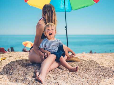 Mother with toddler under parasol on beach