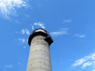 Old lighthouse tower against blue sky and white clouds, view from below