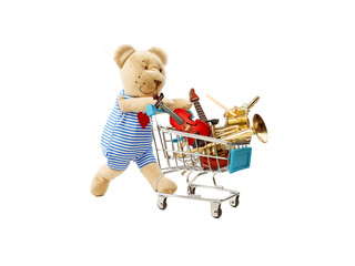 A toy bear is pushing a shopping trolley with a lot of musical instruments. Isolated on white....