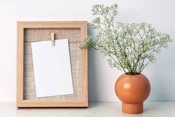 Desk at an empty white wall with a wooden frame with copy space and a vase with white fine flowers