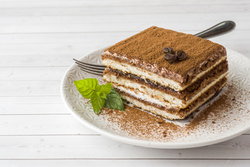 Delicious Tiramisu cake with coffee beans and fresh mint on a plate on a light background