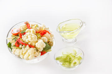 Fresh salad of cauliflower with tomatoes, broccoli, olives, sweet pepper, greens, celery and a glass nipple on a white background