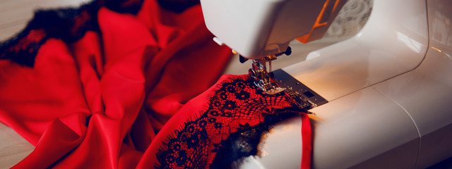 Red silk top with black laces lies on a sewing machine. Process of sensual lingerie making.