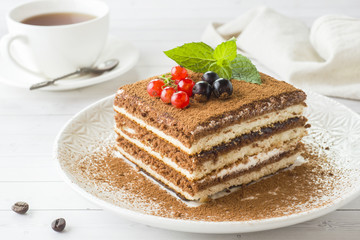 Delicious Tiramisu cake with fresh berries and mint on a plate on a light background. Breakfast with a Cup of coffee.
