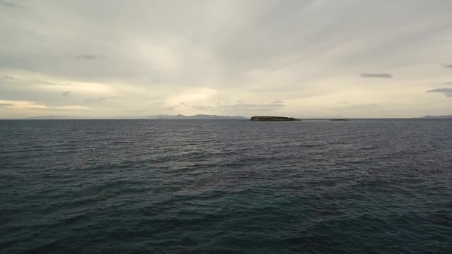 Flying over the sea on a cloudy day. Small island on the horizon.