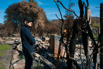 Man owner checking burned and ruined house and yard after fire, consequences of fire disaster accident. Ruins after fire disaster.