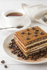 Delicious Tiramisu cake with coffee beans on a plate and a Cup of coffee on a light background
