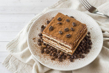 Delicious Tiramisu cake with coffee beans on a plate on a light background