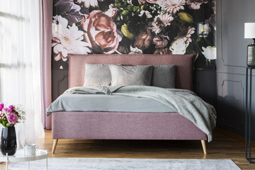 Grey sheets on pink bed in feminine bedroom interior with flowerss print on the wall. Real photo - obrazy, fototapety, plakaty