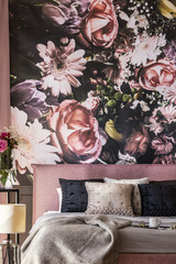 Flowers wallpaper above pink bed with grey and black pillows in feminine bedroom interior. Real...