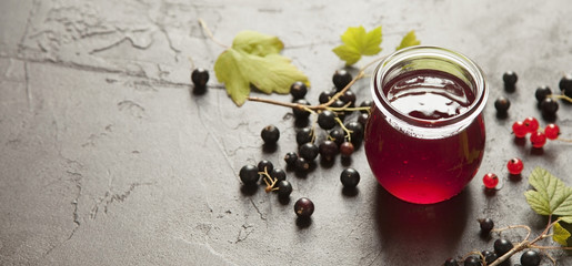 Jar of berry jam with fresh black and red currant on dark background.