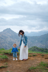 Young beautiful mother and her little daughter walking on the hill in mountains. Scenic mountain view. Dark clouds