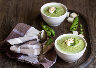 Green pea soup in bowls with spinach and cream on wooden rustic cutting board.