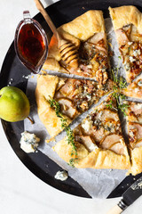 Homemade rustic galette with pears, blue cheese, walnuts and honey on light background. Gallette with a buttery crust and sweet fruit filling. Rustic style.