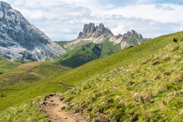 Naklejka premium Italian Dolomites Landscape. Light after rain in Dolomites. Rocky peaks in the background surrounded by rain clouds. Mountain valley with layers of forest and mountains. Aerial view path trail hikeing