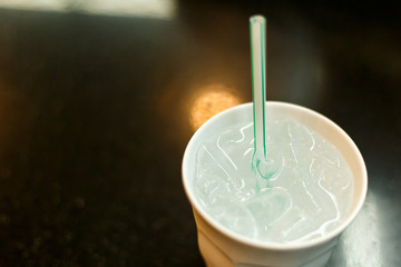 Ice and cold water in white glass with straw put on the black table