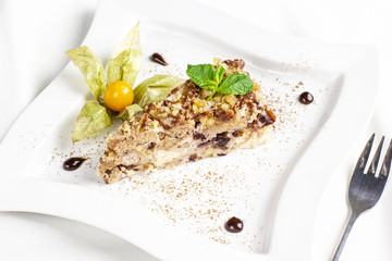 The piece of cake with nuts, dried fruits and physalis on white plate