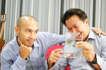 Two asian guys are seeing betta fish in the glass and very happy