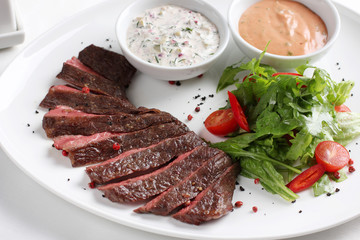 Beef steak, medium rare, with fresh vegetables, herbs and sauce on a white plate