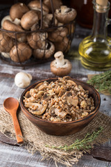 Buckwheat porridge with mushrooms in wooden plate on rustic background