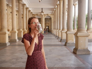 Woman in a summer dress with the spa sipping jug at the Karlovy Vary spa colonnade.