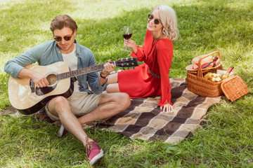 handsome boyfriend playing acoustic guitar for girlfriend at picnic