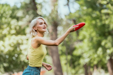 attractive girl throwing frisbee disk in park - obrazy, fototapety, plakaty