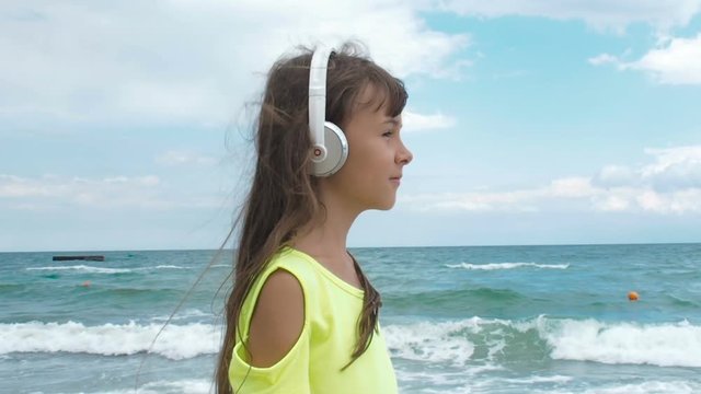 The girl in the headphones is walking along the beach. A little girl listens to music for a walk.