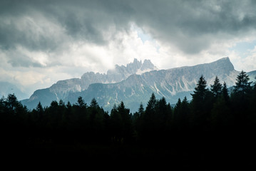  Italian Dolomites landscape. Light after rain in Dolomites. Rocky peaks in the background surrounded by rain clouds. Layers of forest and mountains ridge.  Rocky Mountains Dolomiti. Storm rain over r