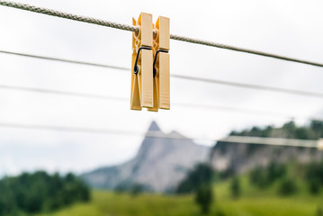 Clothes pins on a clothes line rope. clothespins hanging hook. Clothes pins lined up on a wire. Fresh green meadow and mountains on the background. Wooden clothes pins on a string outside laundry - obrazy, fototapety, plakaty