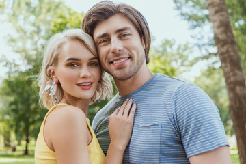 Fototapeta premium smiling couple hugging and looking at camera in park