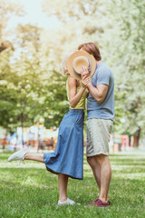 couple kissing and hiding faces with straw hat in park