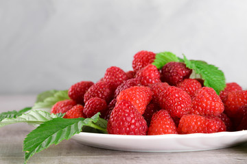 Red fresh raspberries on white rustic wood background. Plate with natural ripe organic berries with green leaves.flat lay with copy space