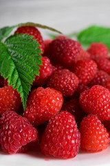 Red fresh raspberries on white rustic wood background. Plate with natural ripe organic berries with green leaves.flat lay with copy space