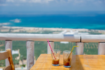 Two little glasses with cold cappuccino with tubule on a wooden table in Greece cafe in summertime