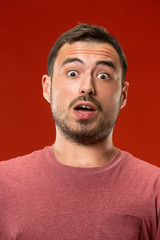 Obraz premium The young attractive man looking suprised isolated on red