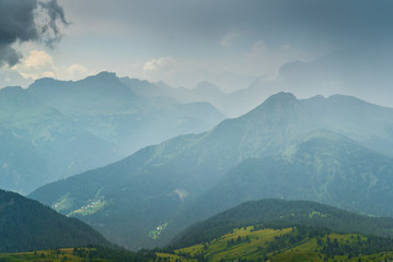 Fototapeta premium Italian Dolomites Landscape. Light after rain in Dolomites. Rocky peaks in the background surrounded by rain clouds. Mountain valley with layers of forest and mountains. Beautiful light in Alps. Italy