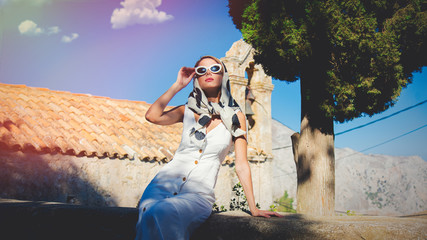 Young girl dressing in 60s style clothes in a village with old church on background. Crete, Greece