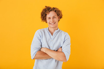 Photo of caucasian cheerful guy 20s with curly hair laughing and standing with arms folded,...