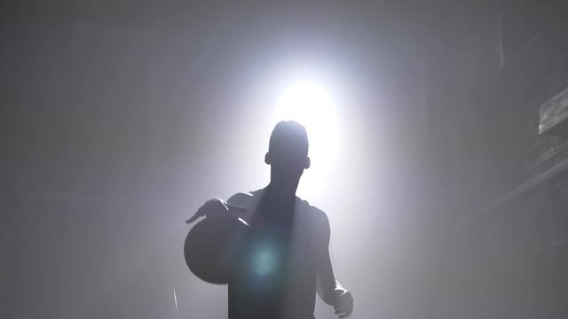 Basketball player silhouette throwing ball in hoop, smoke everywhere, floodlight in background