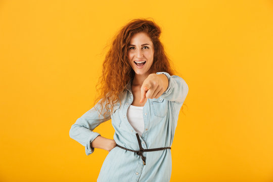 image of joyous european woman 20s pointing finger forward at you with smile, isolated over yellow background