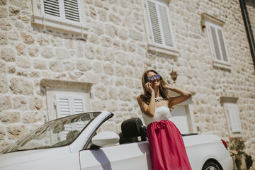 Young woman using mobile phone and standing by cabriolet car
