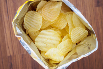 Potato chips in open snack bag close up on table floor