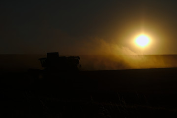 Combine harvester at sunset in the dust of the husks